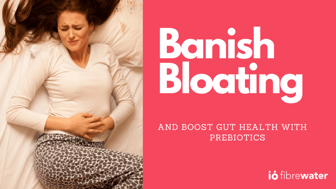 Woman lying in bed holding her stomach in discomfort next to text that says “Banish Bloating and Boost Gut Health with Prebiotics,” promoting ió Gut Health Drink.